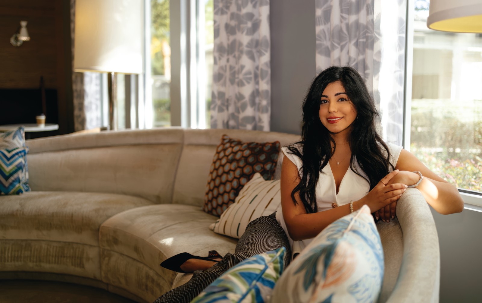 Reflection – Maha Chaudhry Maha Chaudhry seated on a curved sofa in a sunlit living room